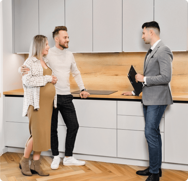 A man is talking to a pregnant woman and a man in a kitchen.