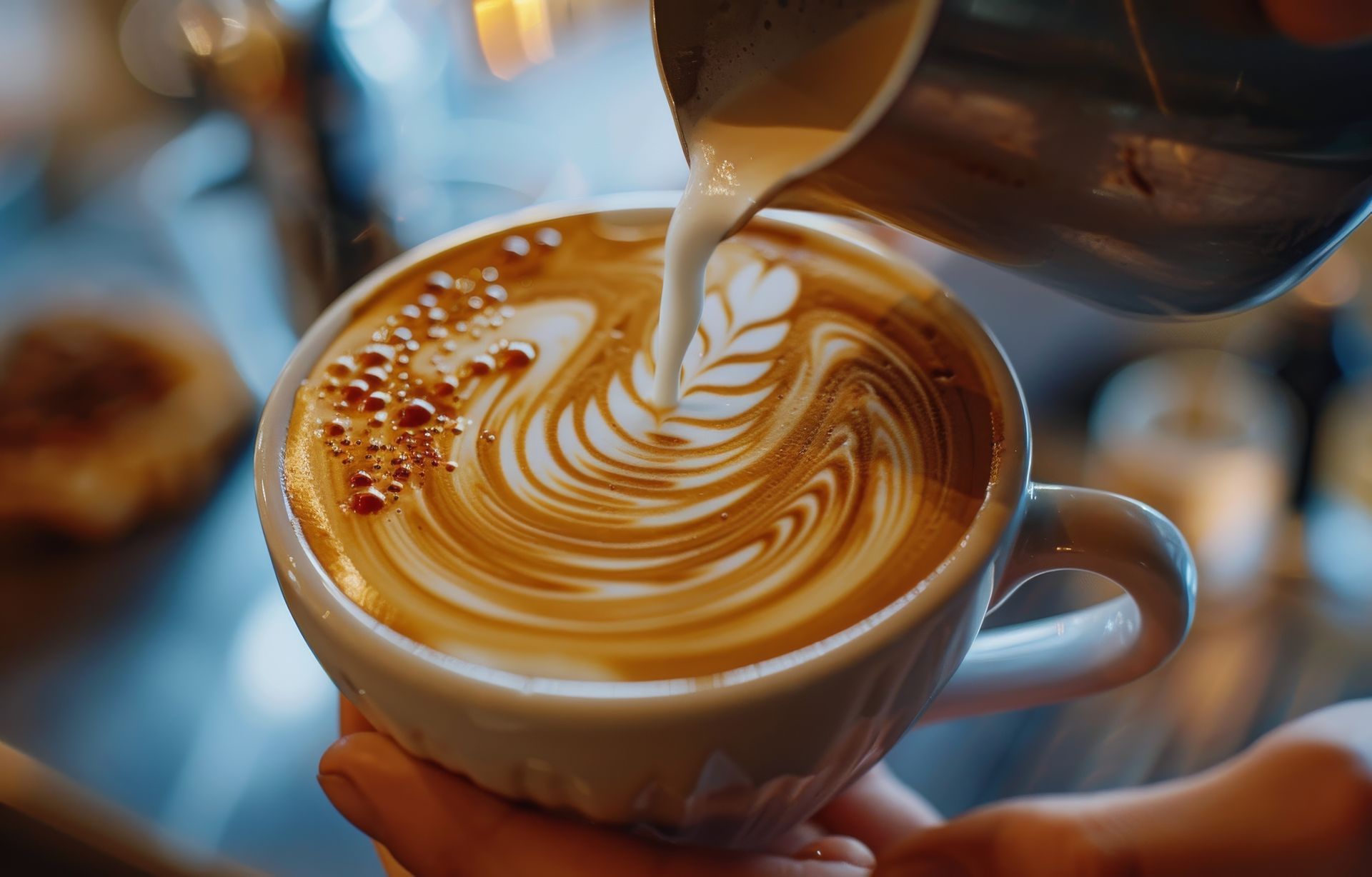 Barista pouring milk into a coffee cup, creating latte art.