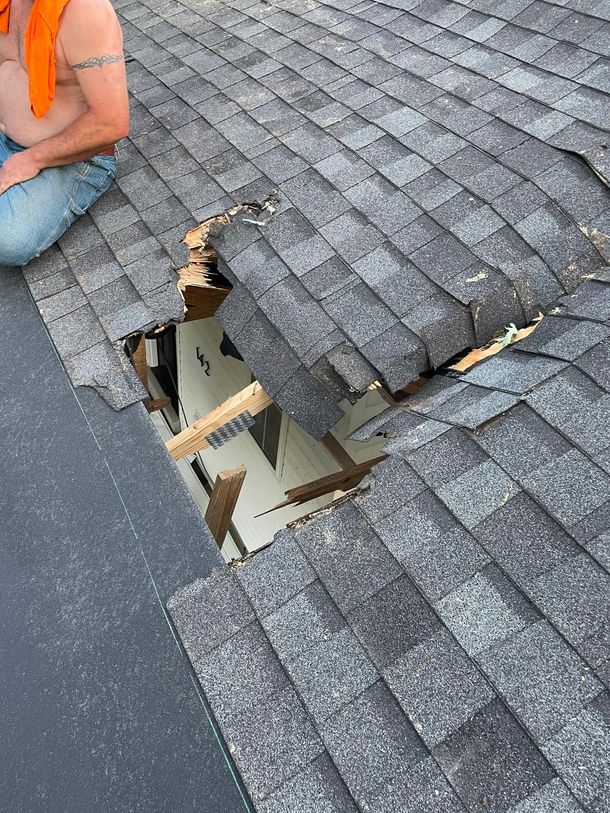 A man is kneeling on a roof with a hole in it.