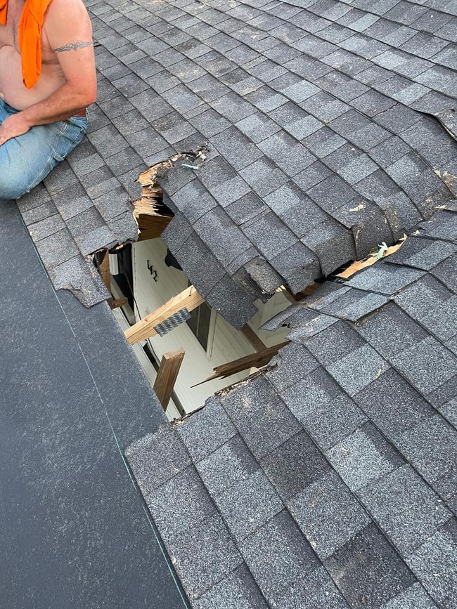 A man is kneeling on a roof with a hole in it.