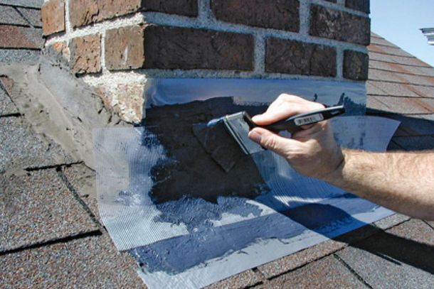 A person is painting a brick chimney on a roof