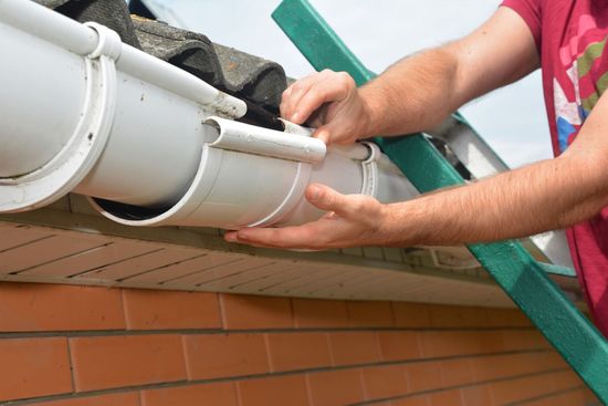 A man is fixing a gutter on the roof of a house.