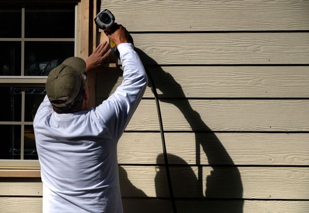 A man is using a drill to install a window trim on a house.