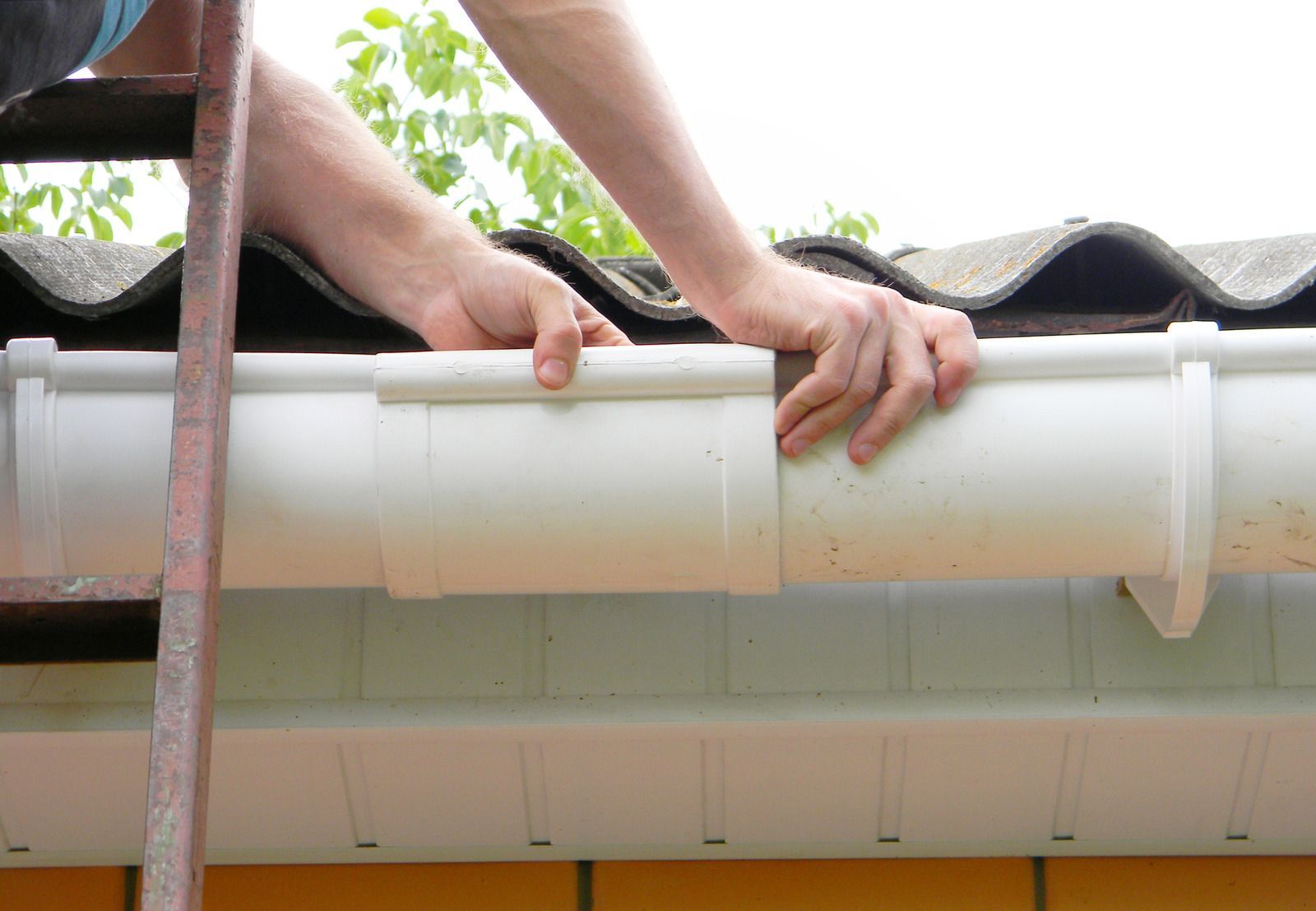 A man is fixing a gutter on the roof of a house.