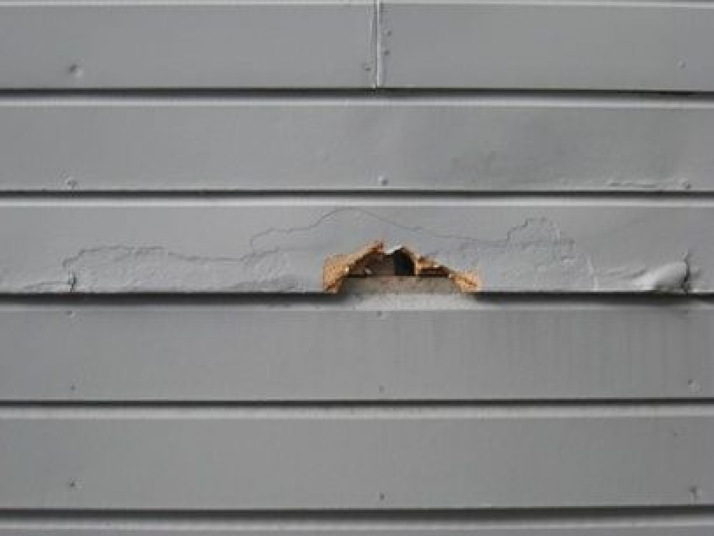 A close up of a gray siding wall with a hole in it.