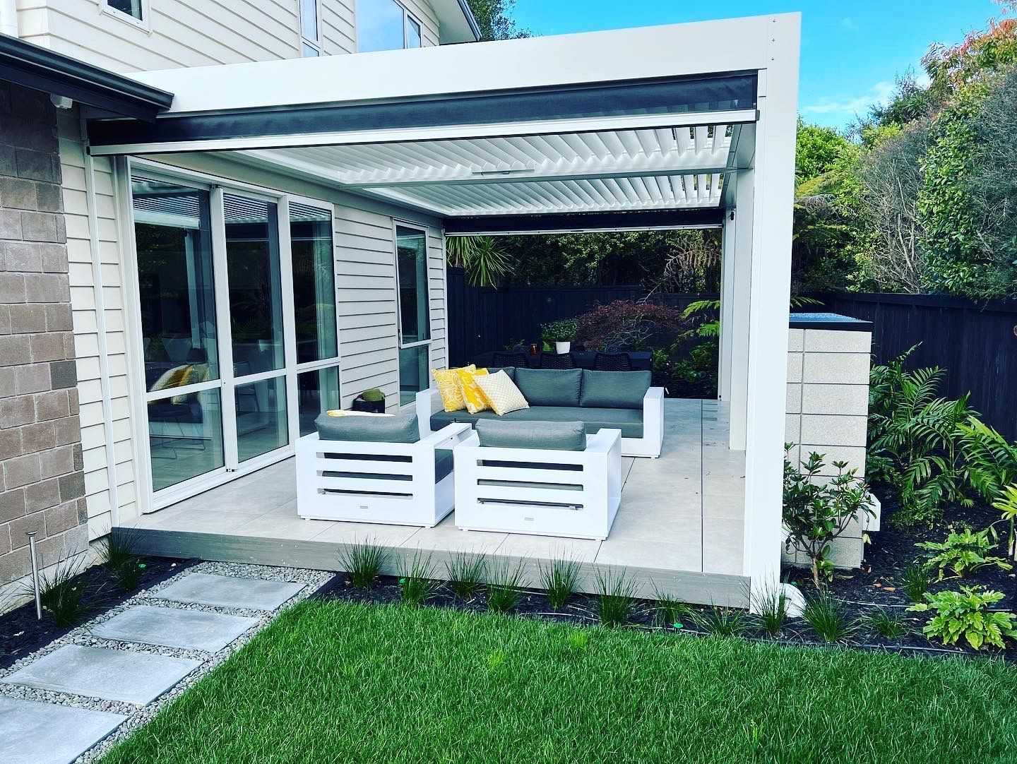 There is a pergola in the backyard with a couch and chairs underneath it.