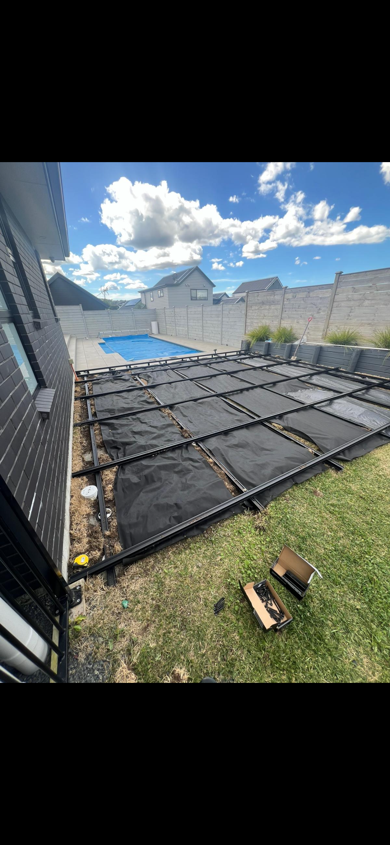 A row of solar panels are sitting on top of a lawn next to a swimming pool.