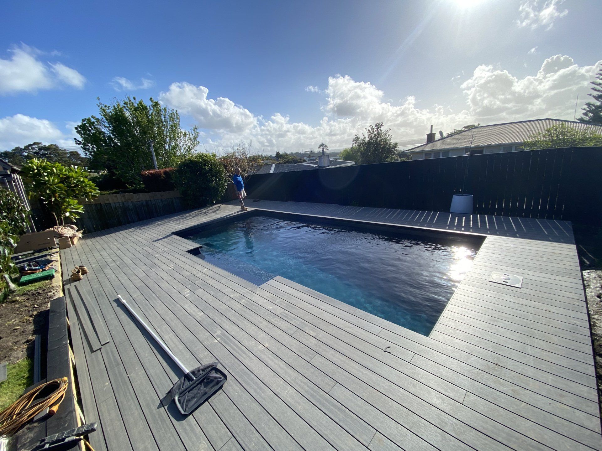 A man is standing next to a swimming pool on a wooden deck.