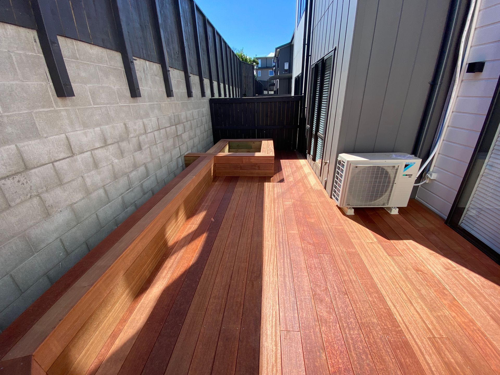 A wooden deck with a bench and an air conditioner.