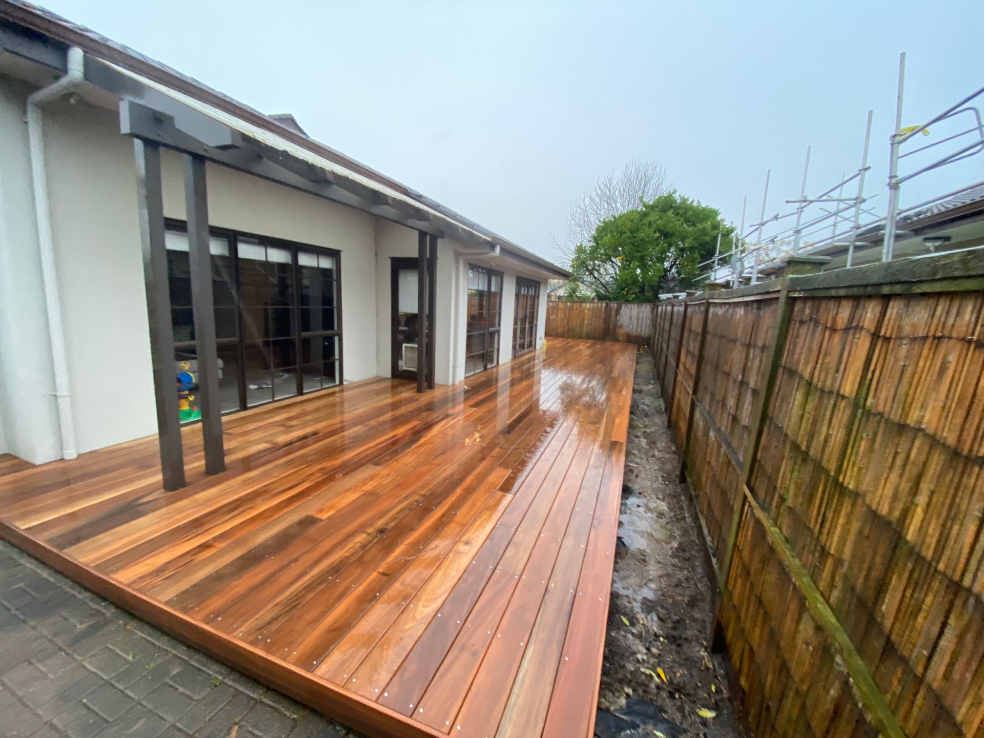 A wooden deck is sitting next to a fence in front of a house.