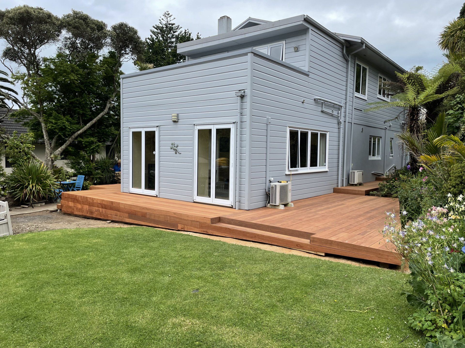 A large gray house with a wooden deck in front of it.