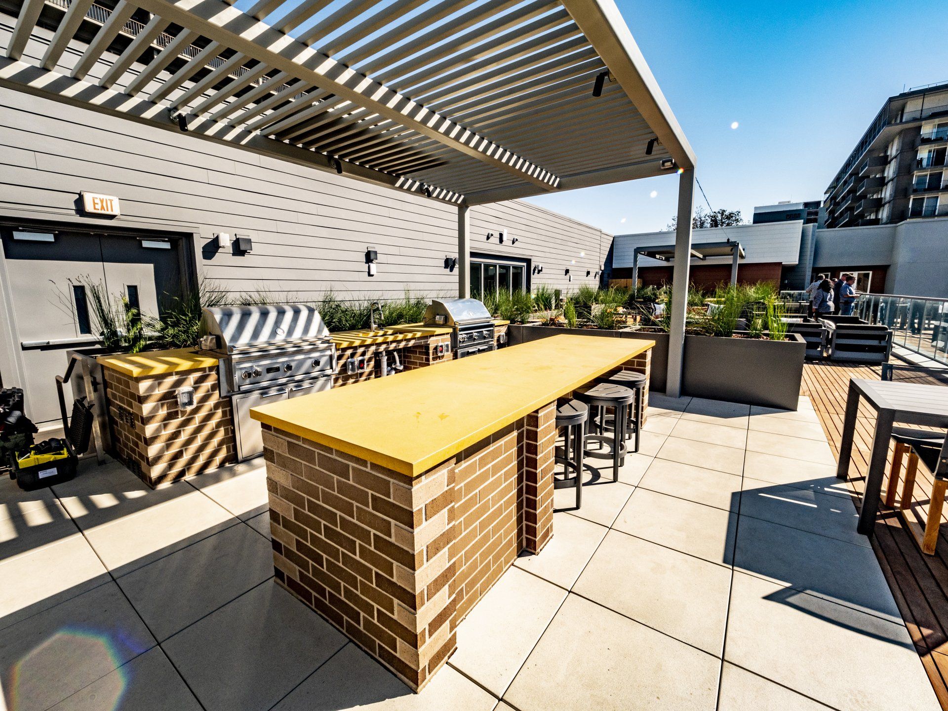 A large brick table with a yellow top sits under a pergola on a rooftop patio at Capitol Towers.