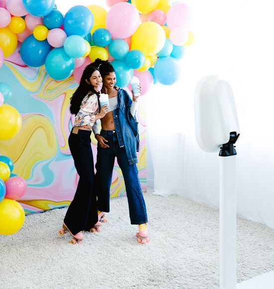 Two women are posing for a picture in front of balloons.