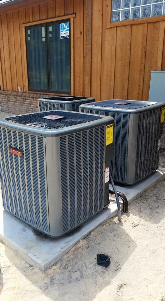 A person wearing dark blue overalls installs a white wall-mounted air conditioning unit. A person wearing dark blue overalls installs a white wall-mounted air conditioning unit.