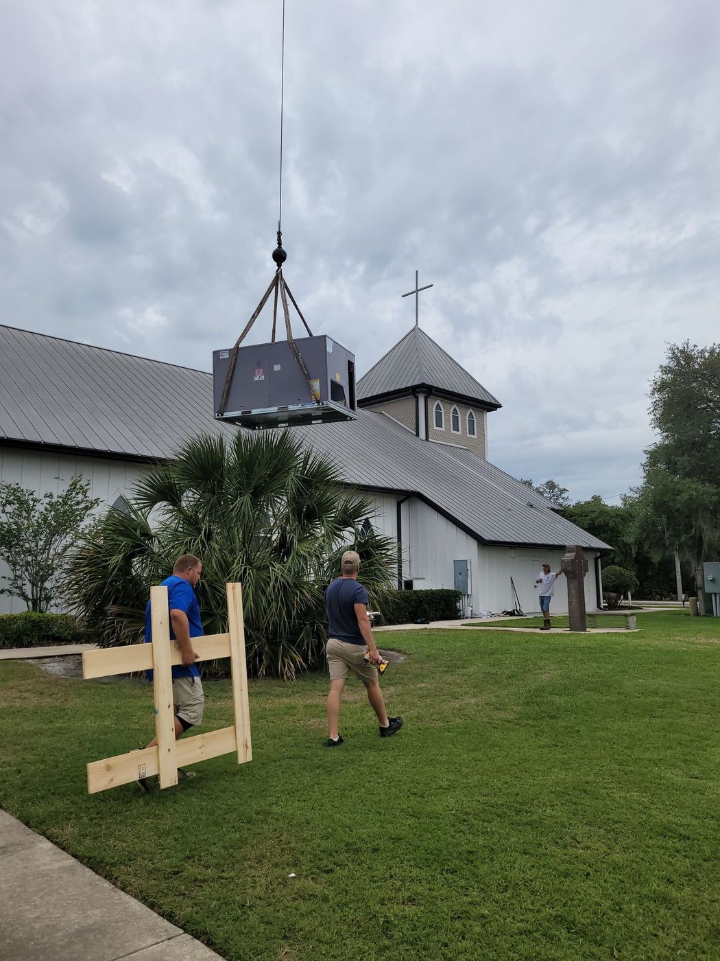 An outdoor air conditioning condenser unit sits on a grass lawn next to a white building with a residential house behind. An outdoor air conditioning condenser unit sits on a grass lawn next to a white building with a residential house behind.