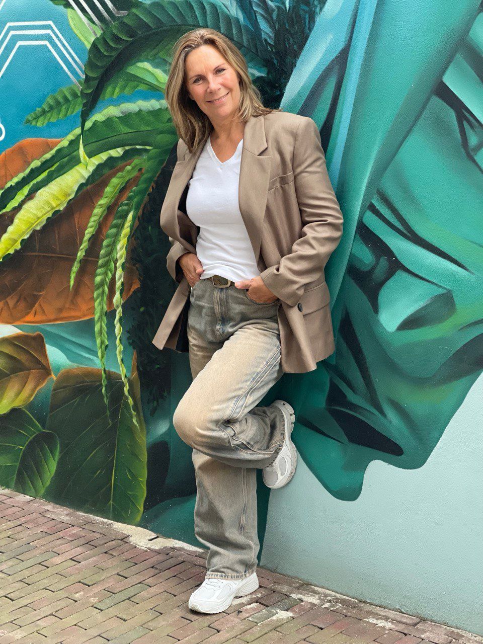 Woman in blazer and jeans leaning against a colorful mural.