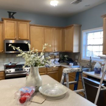 Kitchen with light wood cabinets, blue walls, stainless steel appliances, and a vase of white flowers.