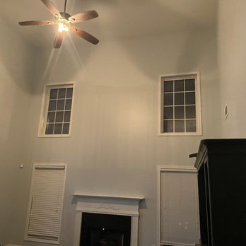 High-ceilinged room with two windows, a fireplace, and a ceiling fan. The walls are light blue.