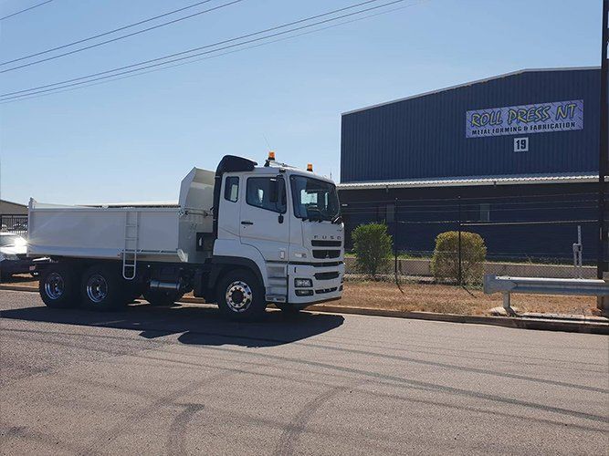 A White Dump Truck is Parked on the Side of the Road in Front of a Building — Roll Press NT In Tivendale, NT