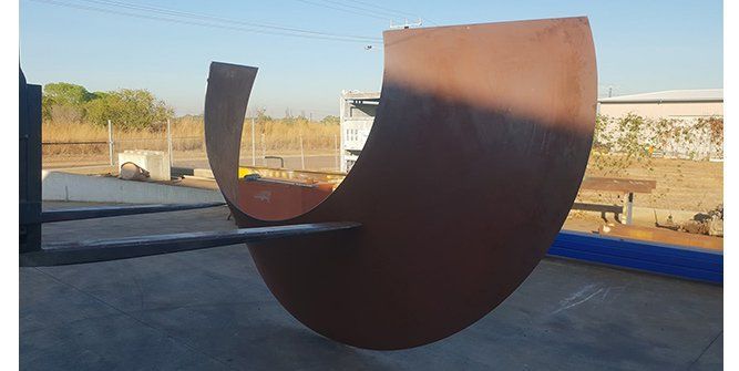 A large metal sculpture is sitting on the ground in a parking lot.