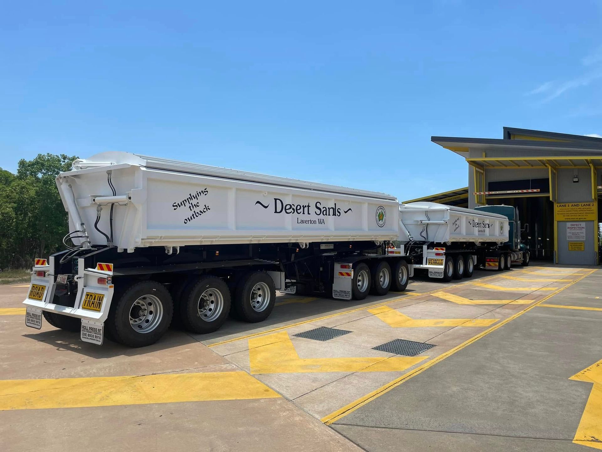 A White Truck With a Flatbed Trailer Attached to It is Parked on the Side of the Road — Roll Press NT In Tivendale, NT