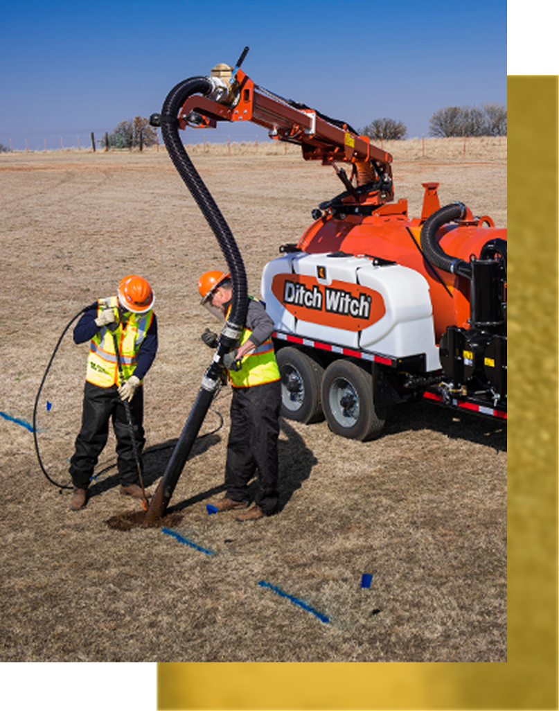 Two workers using a Ditch Witch vacuum excavator in a field. One holds a nozzle, the other a hose.