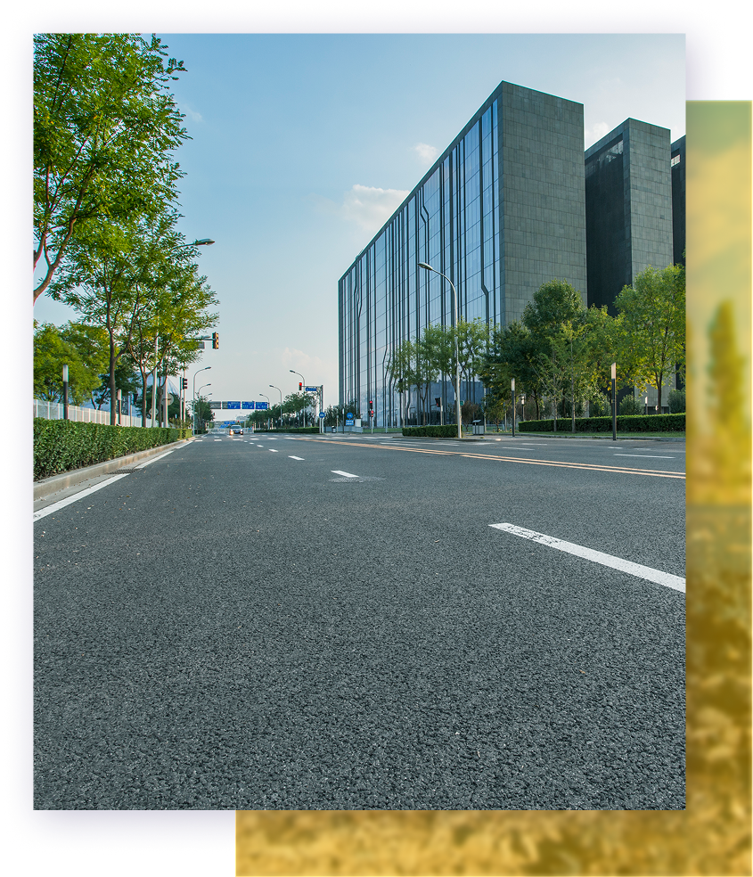 Empty asphalt road with modern office buildings, trees, and blue sky.