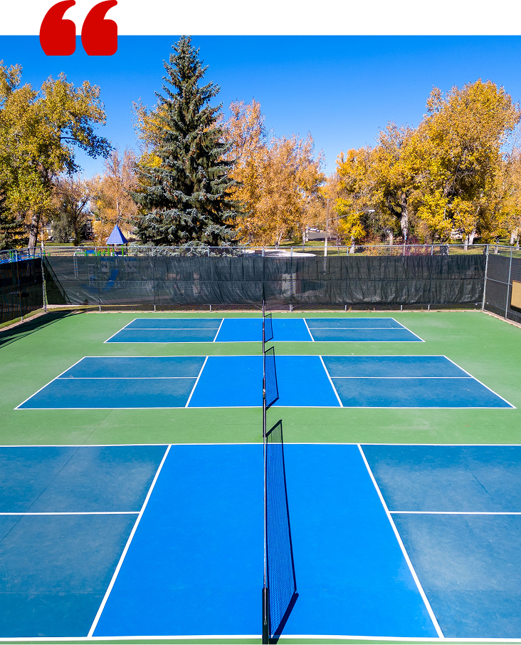 Snowplow clears snow from a road in front of a yellow building and trees.