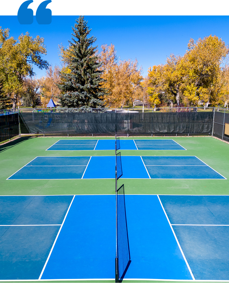 Snowplow clears snow from a road in front of a yellow building and trees.