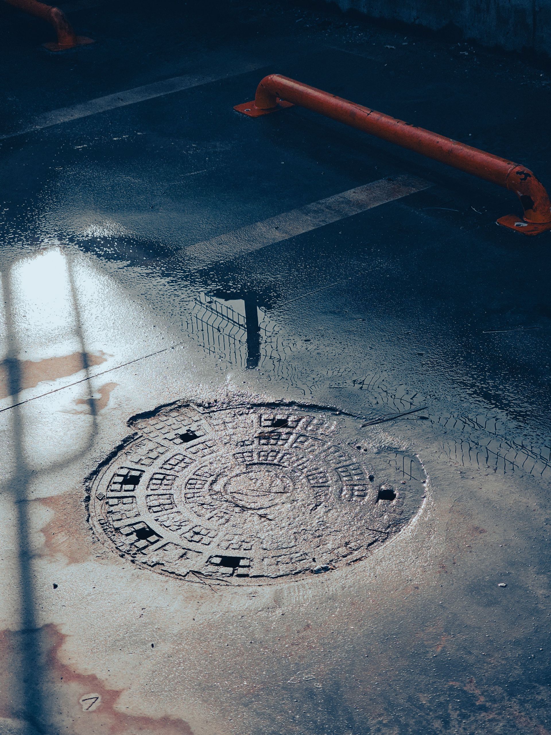 Wet street with a round manhole cover and red curb rail.