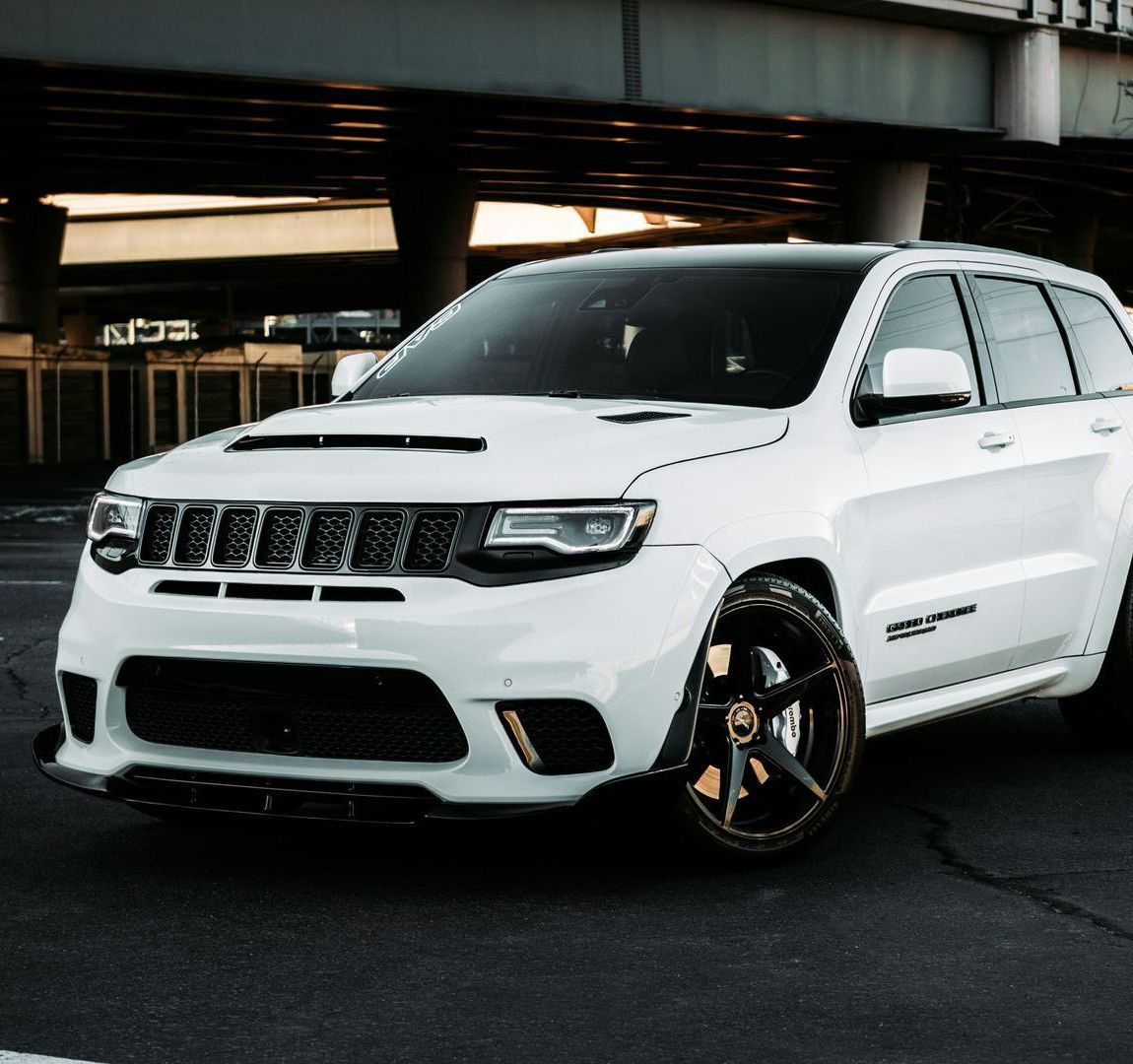 A white jeep grand cherokee is parked under a bridge