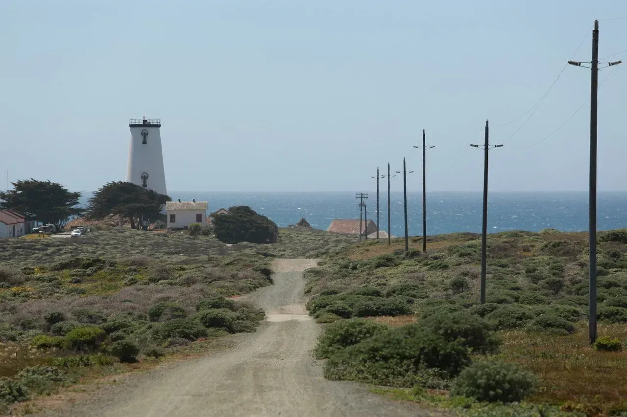 Uma estrada de terra com um farol ao fundo