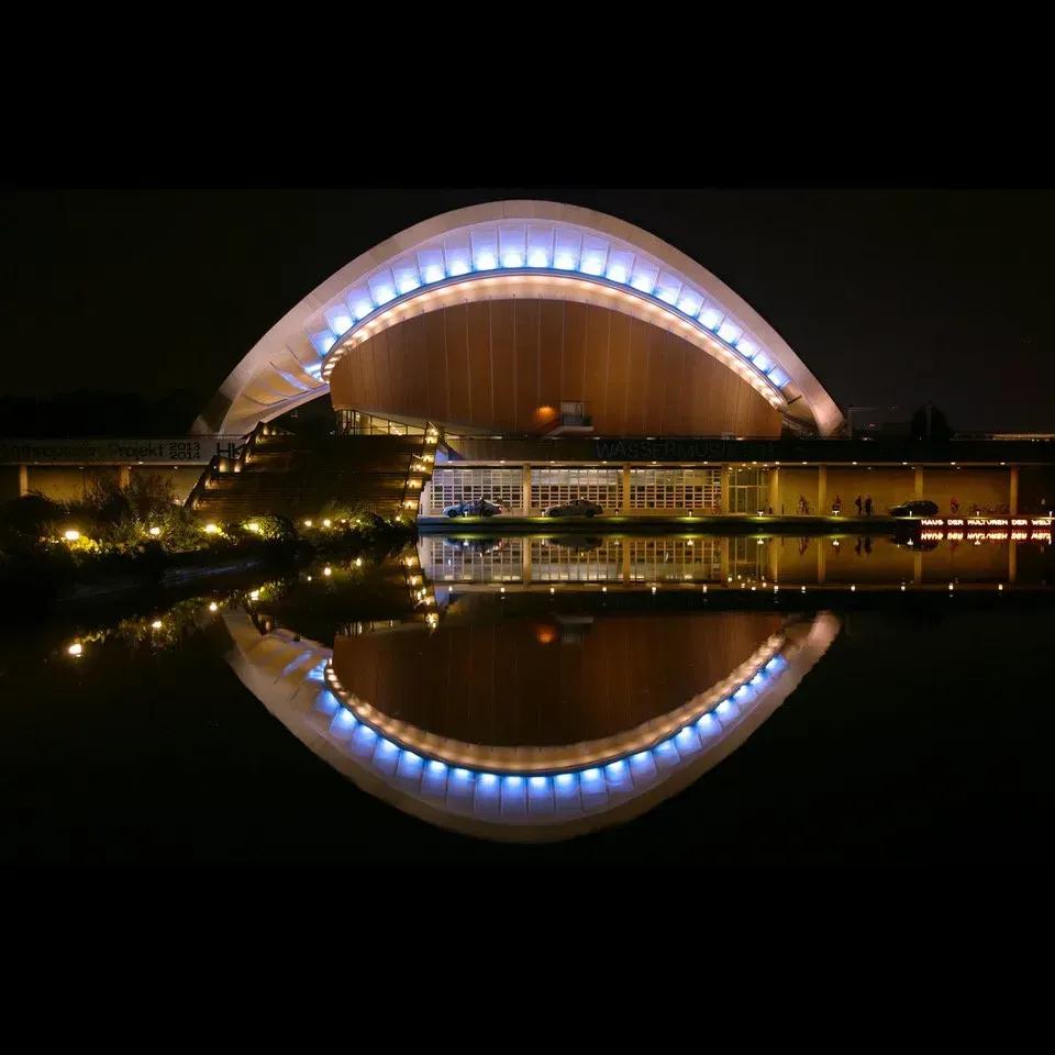 Um grande edifício é iluminado à noite e refletido na água