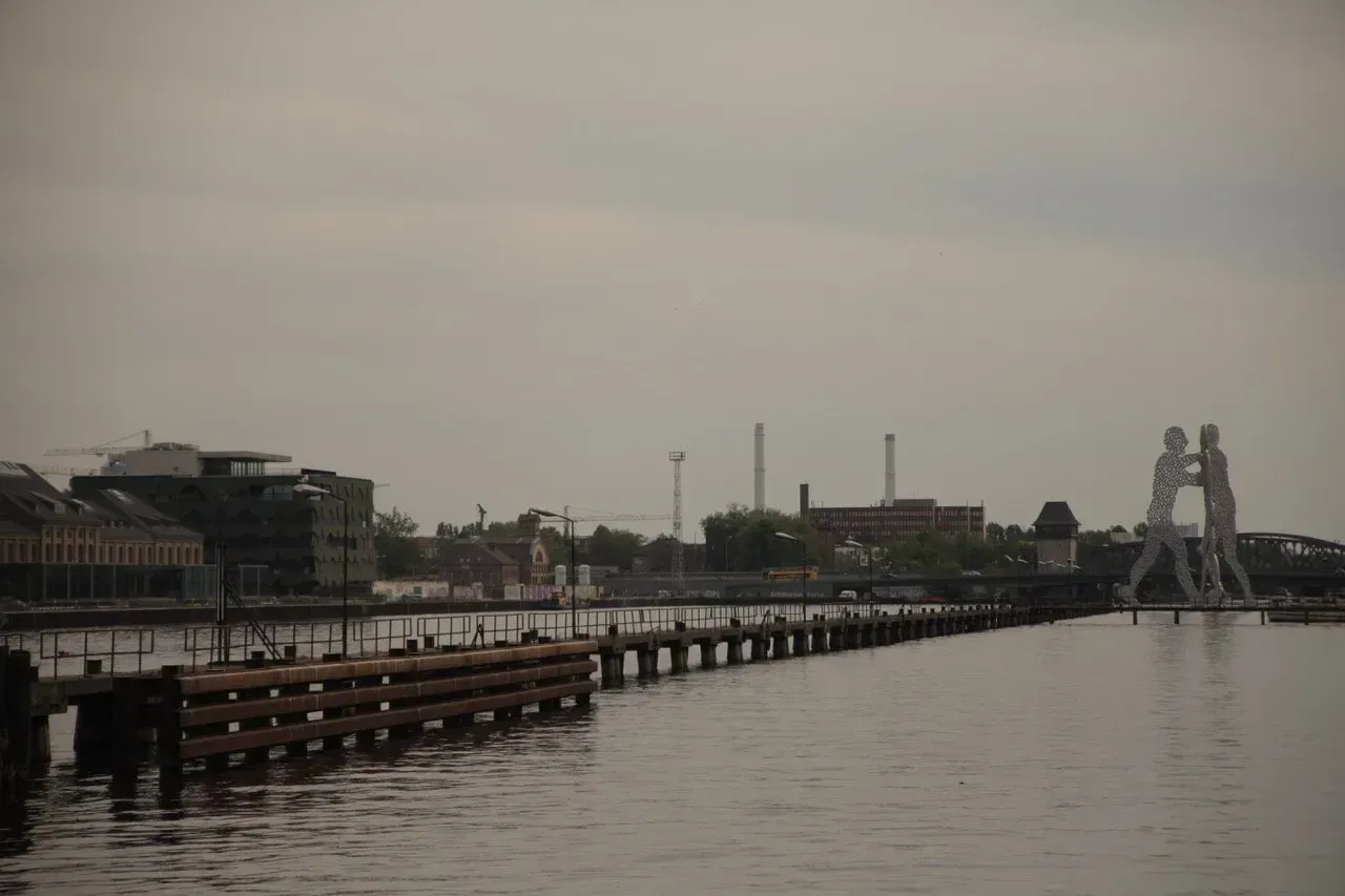 Um píer que leva a um corpo d'água com uma estátua ao fundo.
