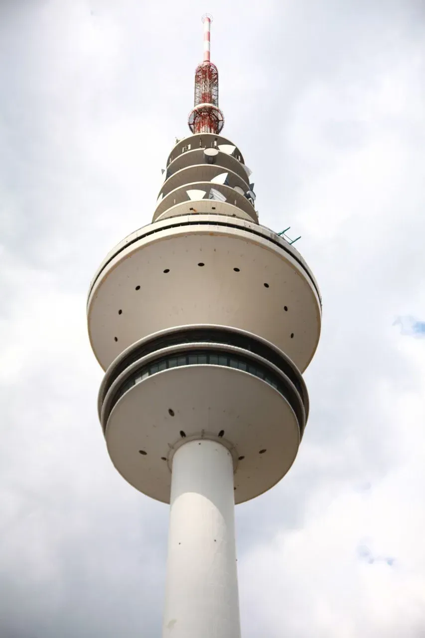 Uma torre alta e branca com um topo vermelho contra um céu nublado