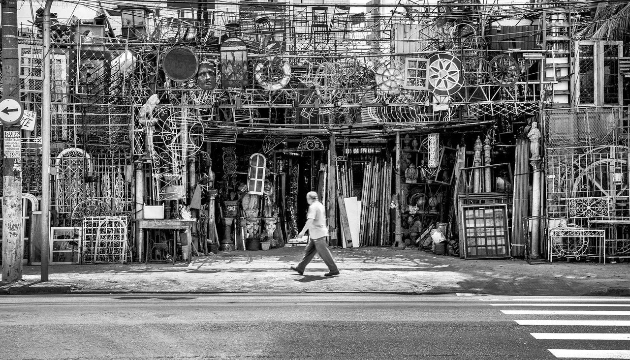 Uma foto em preto e branco de um homem caminhando pela rua em frente a um prédio.
