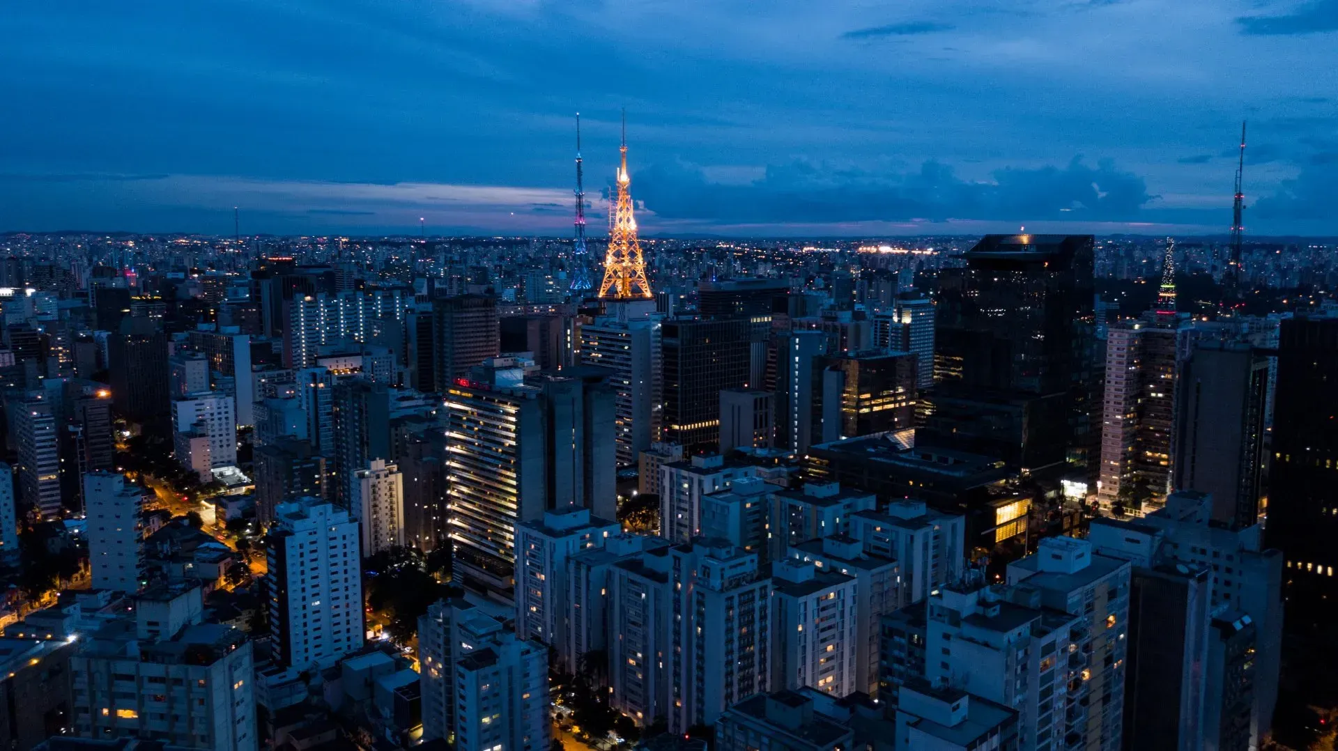 Uma vista aérea de uma cidade à noite com uma torre ao longe.