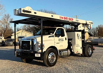 A white truck with a ladder on top of it is parked in a gravel lot.