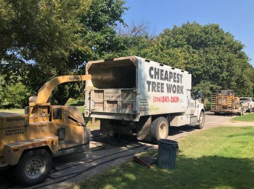 A cheapest tree work truck is parked in a driveway next to a tree chipper.