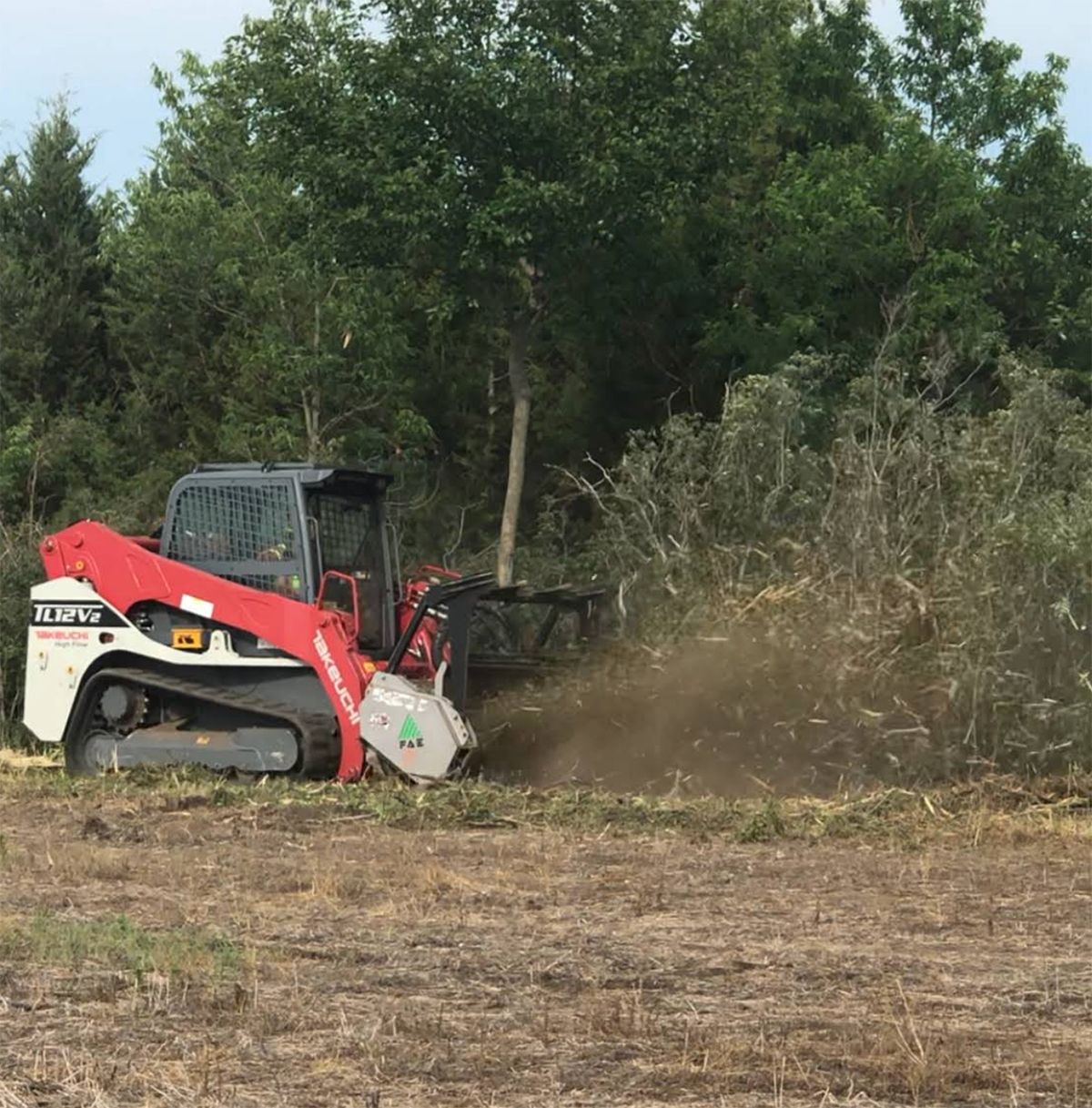 A bulldozer is clearing brush in a field with trees in the background