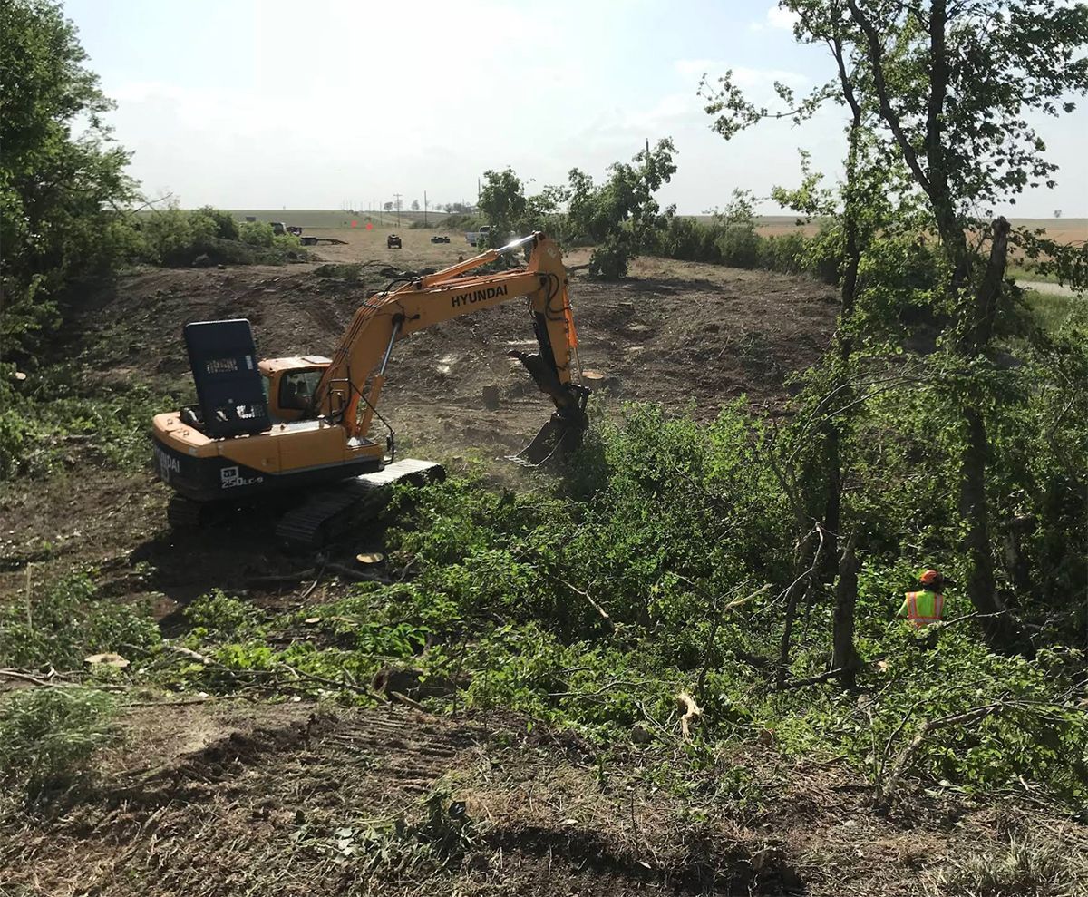 A yellow excavator is sitting in the middle of a field surrounded by trees.