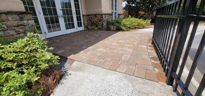 A brick walkway leading to a house with a fence in front of it.