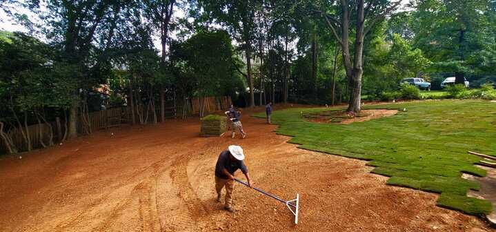 A man is raking dirt in a yard with a rake.