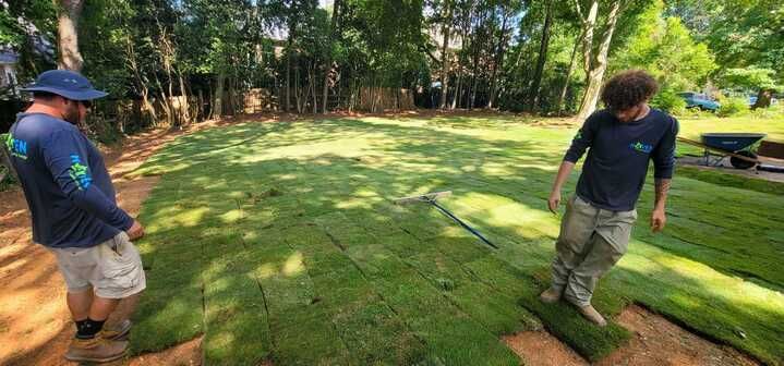 Two men are working on a lush green lawn.