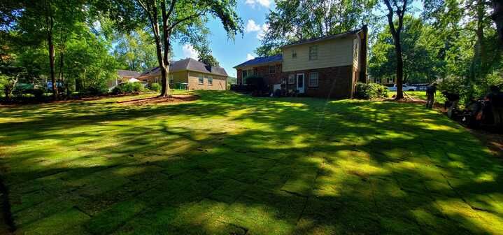 A large lush green lawn in front of a house surrounded by trees.