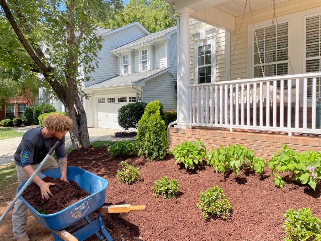 A man is loading mulch into a wheelbarrow in front of a house.