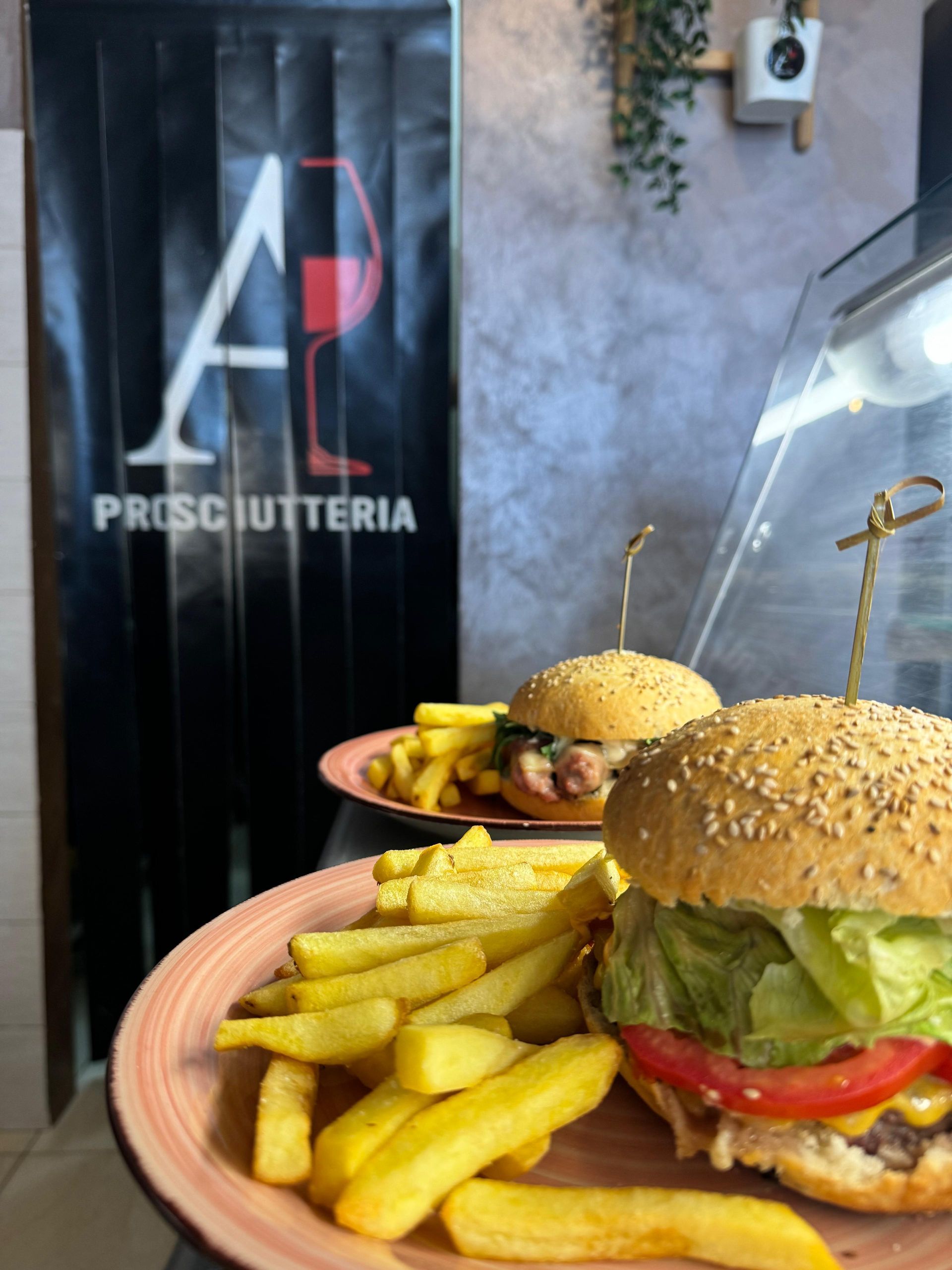 Due hamburger e patatine fritte su un piatto davanti al cartello di una prosciutteria