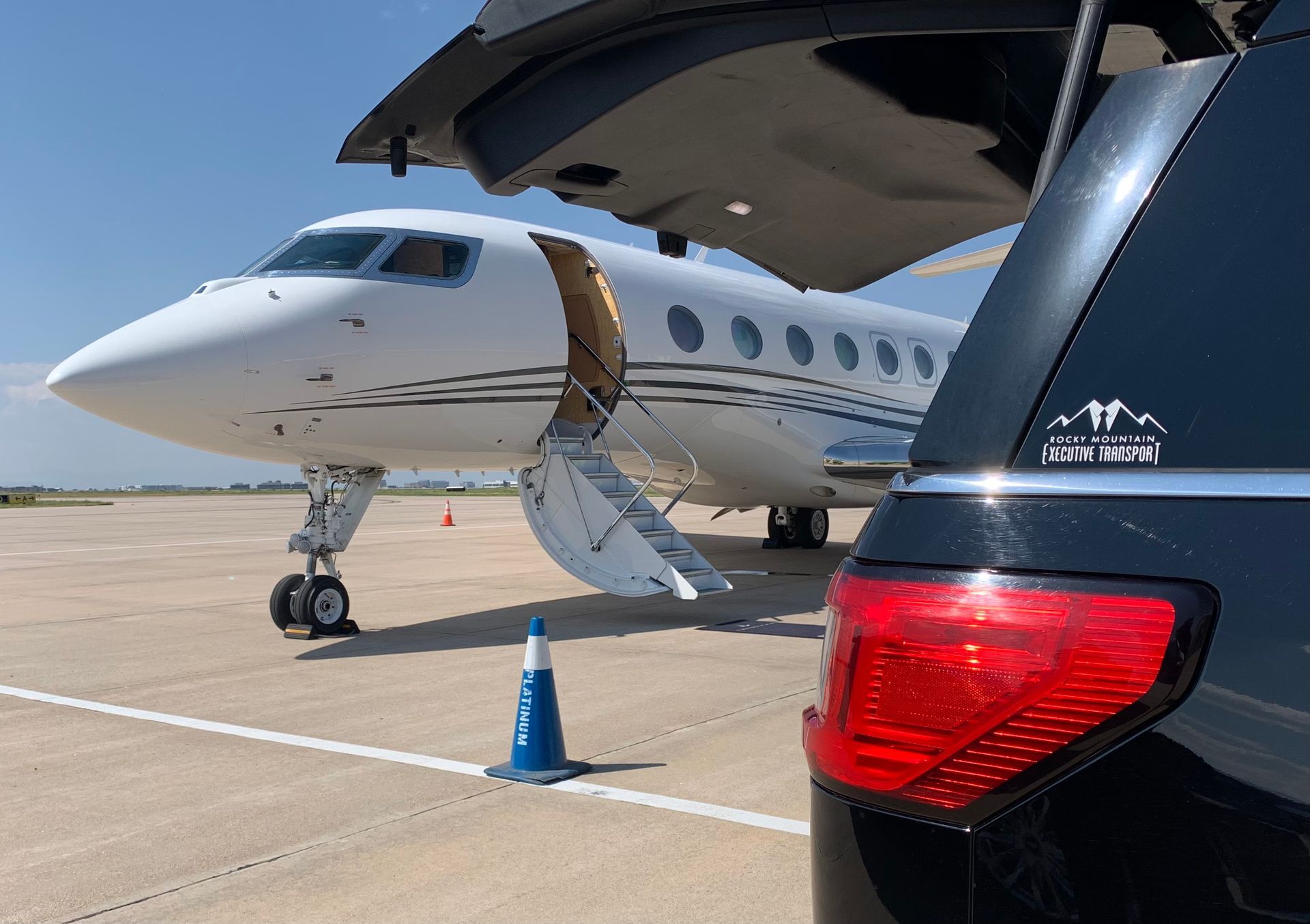 A private jet is parked on the tarmac next to a car.