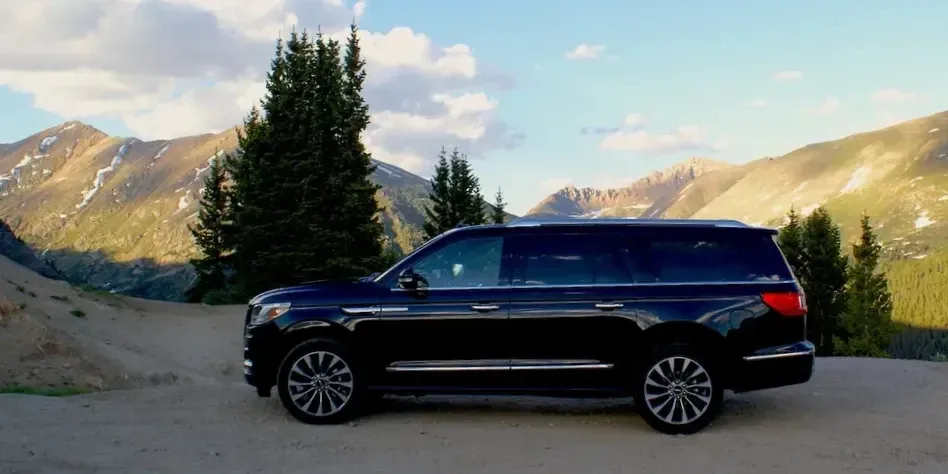 A black suv is parked on a dirt road in front of a mountain.