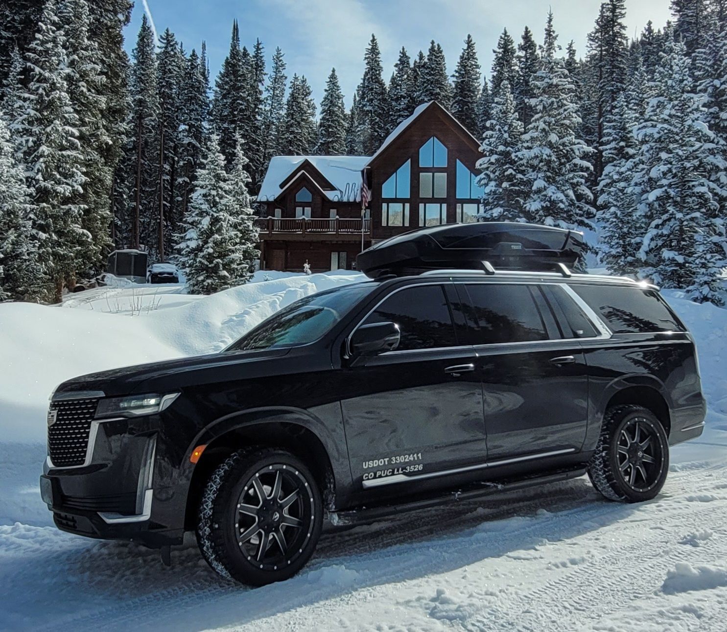 A black suv is parked in the snow in front of a house